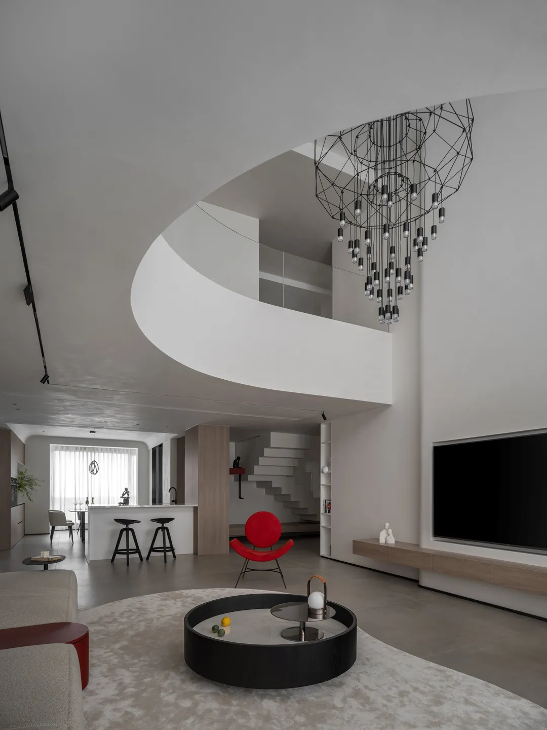 A modern living room with minimalist decor, featuring a red armchair, round black coffee table, and geometric chandelier.