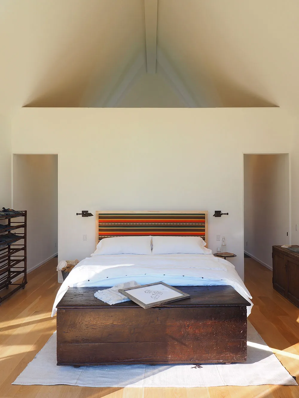 A minimalist bedroom featuring a wooden headboard and white linens on a large bed.