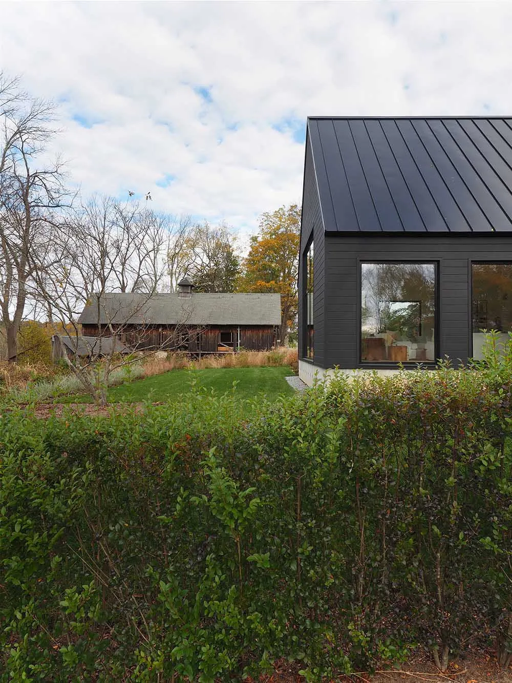 A modern house with a black-clad exterior featuring a metal roof and large windows.