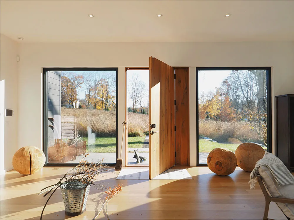 An open wood door in a minimalist entryway with large windows showcasing a fall landscape.