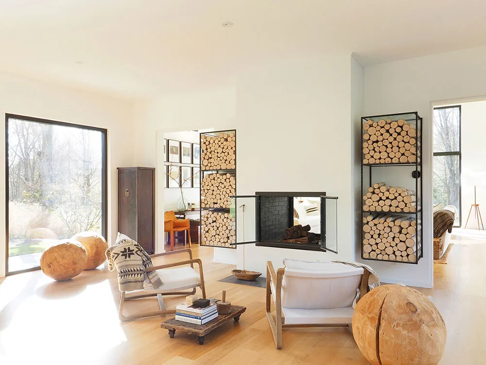 A modern minimalist living room featuring a double-sided fireplace, floor-to-ceiling glass windows, and wood furniture.