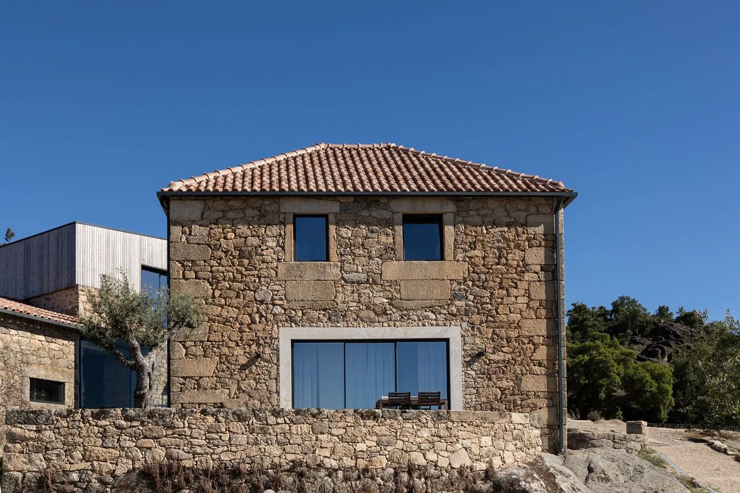 Rustic stone house with tiled roof and large windows.