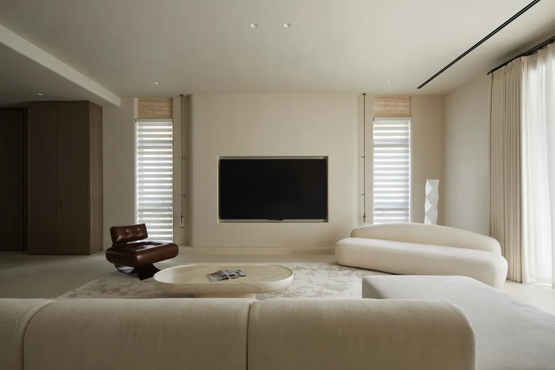 A minimalist living room with a neutral color palette featuring a sleek, curved sofa, a low wooden coffee table, a black flat