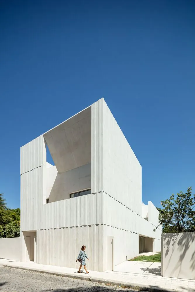 一座現代白色混凝土建築，頂樓有開放空間，背景有樹木。