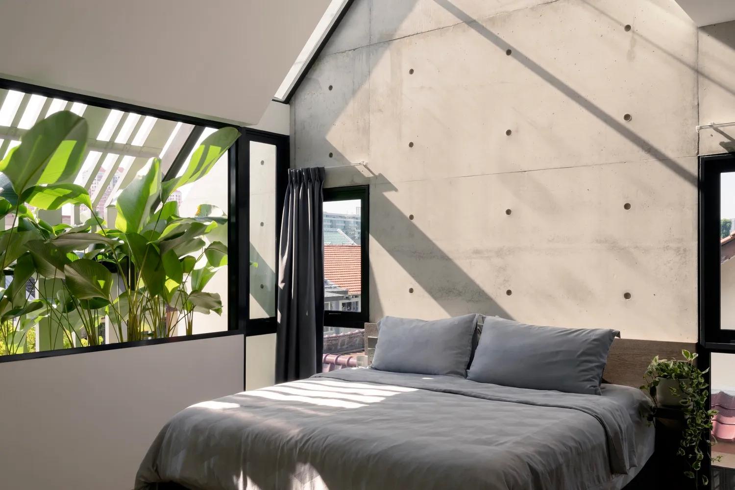 A minimalist bedroom featuring concrete walls and large windows with green plants.