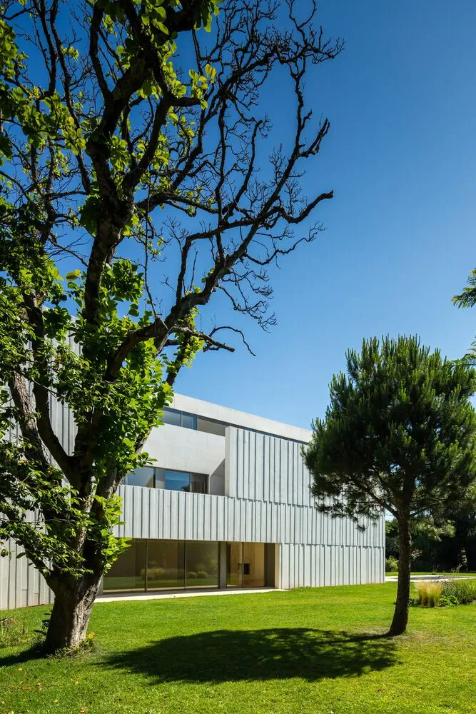 A minimalist residential building with a metal-cladding exterior on a sunny day with green trees in the foreground.