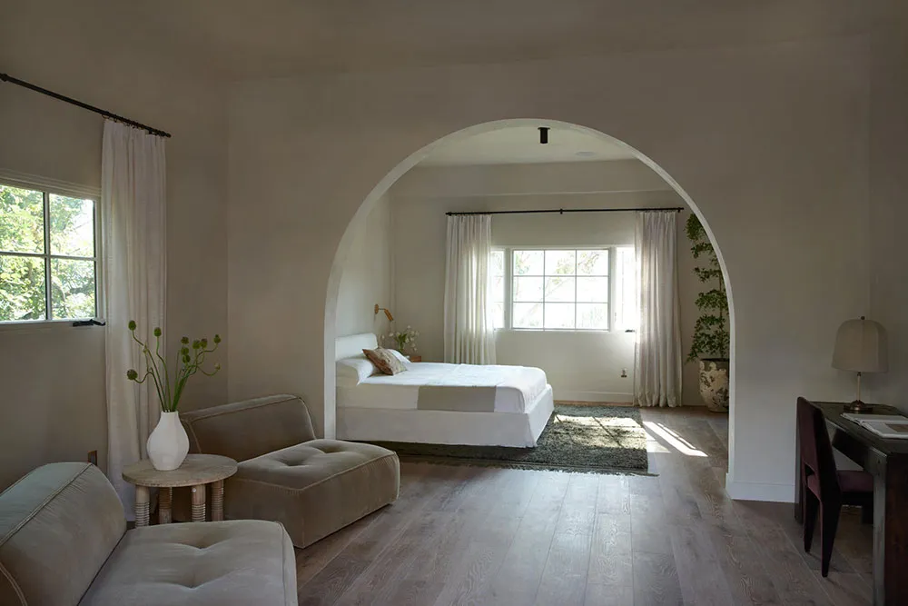 A minimalist bedroom with white furniture and soft lighting.