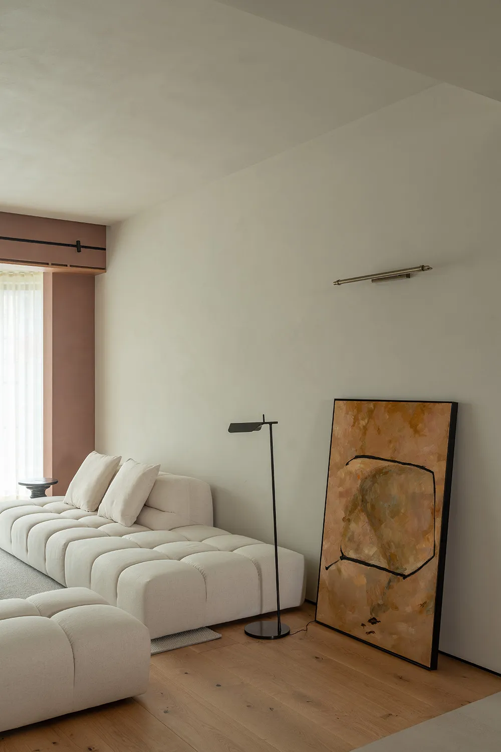 A minimalist living room featuring a cream-colored floor lamp, a white couch with tufted cushions, and an abstract painting i