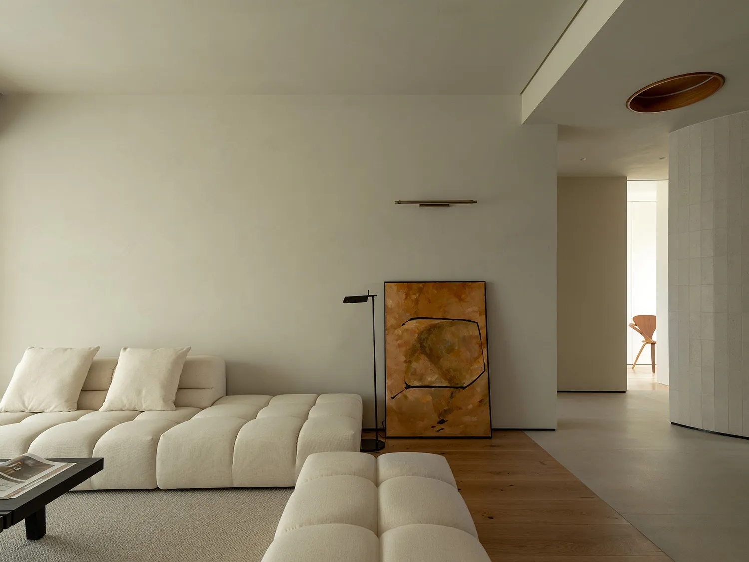A minimalist living room with a white sofa, wooden coffee table, and large abstract painting.