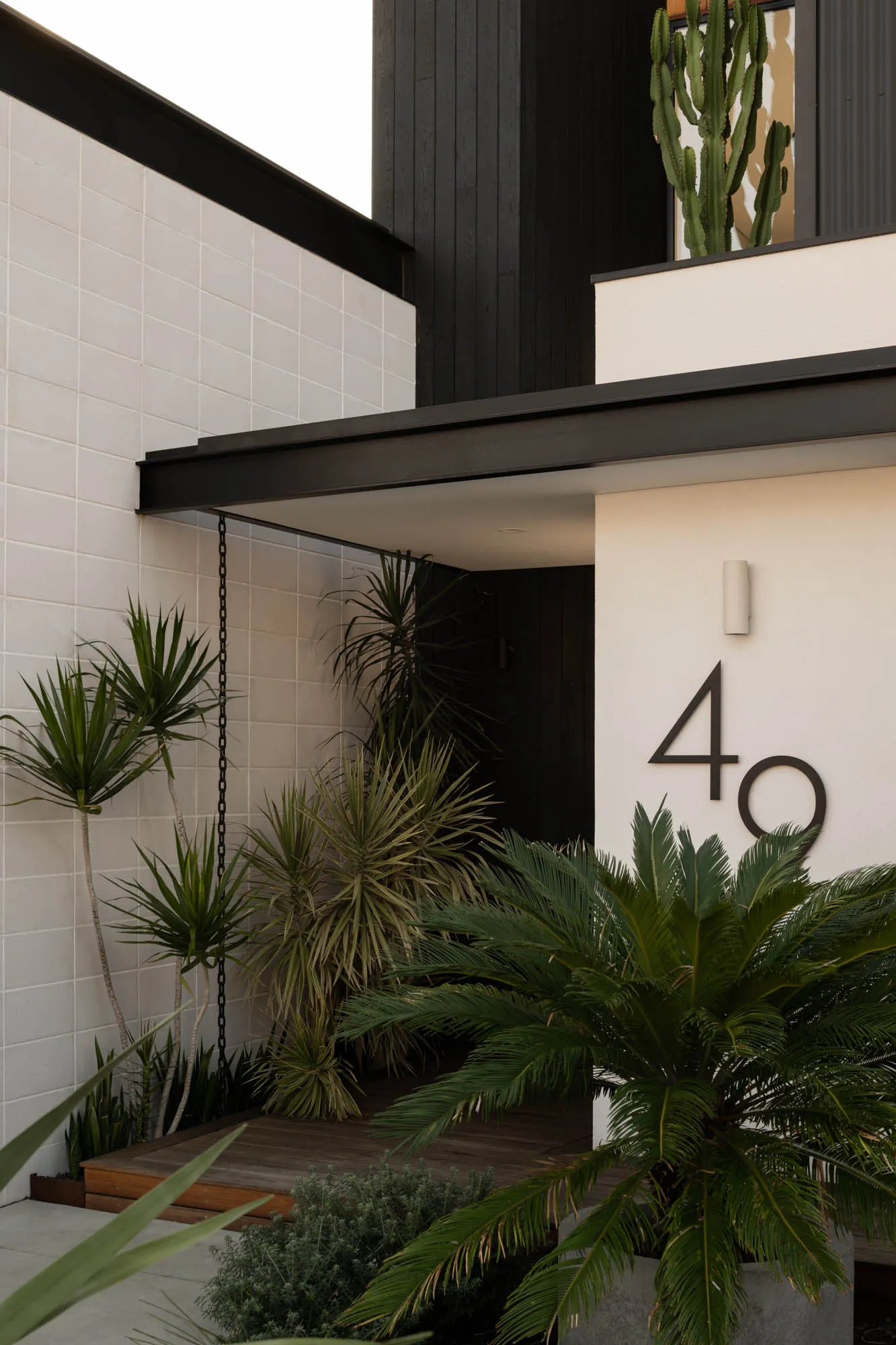 Modern front door entryway featuring concrete, wood, and lush green plants
