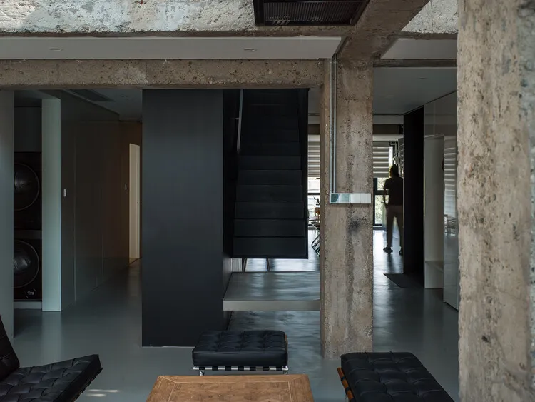 A modern industrial living space with concrete columns, black staircase, and black leather furniture.