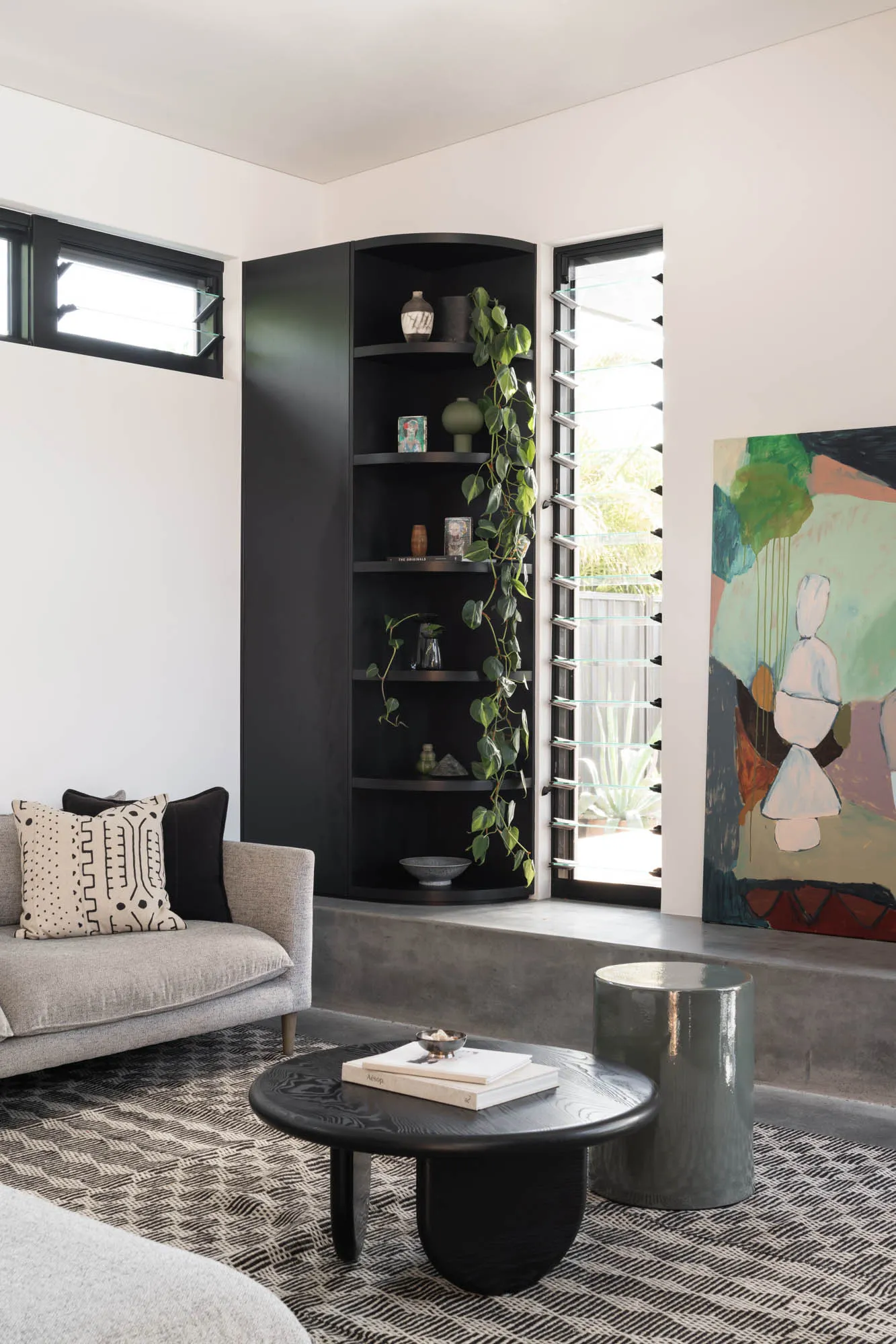 A modern living room featuring concrete walls and plants in corner planters.