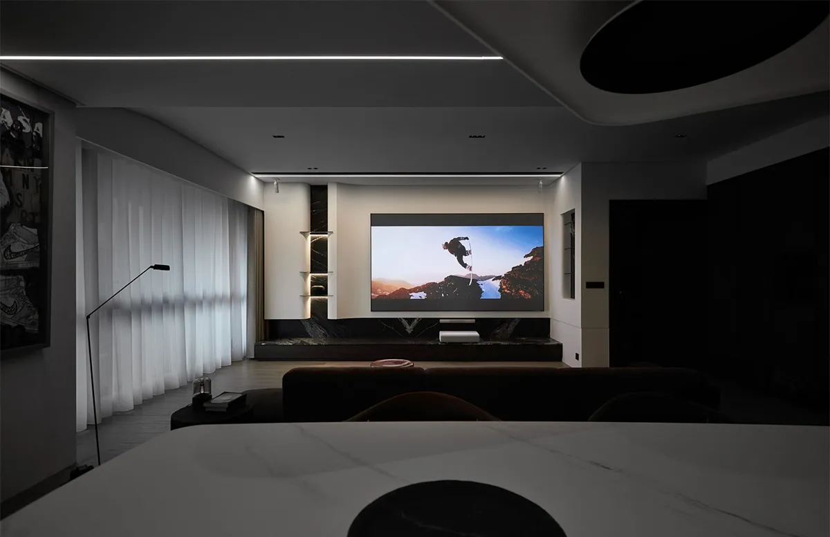 Modern living room with mixed materials, featuring a large screen displaying a person on a snowy landscape.