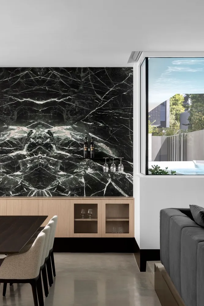A modern kitchen featuring a black marble backsplash, wooden cabinets, and contemporary furniture.