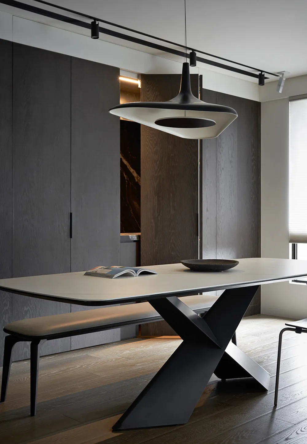 Modern minimalist dining room with a sleek wooden table, metal legs, and minimalist pendant light.