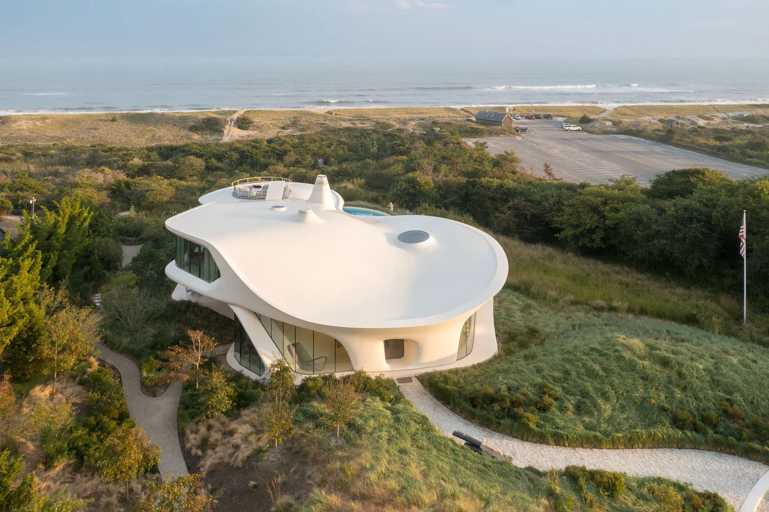 A modern, white stucco and glass residential house with a curved roof and a pool.