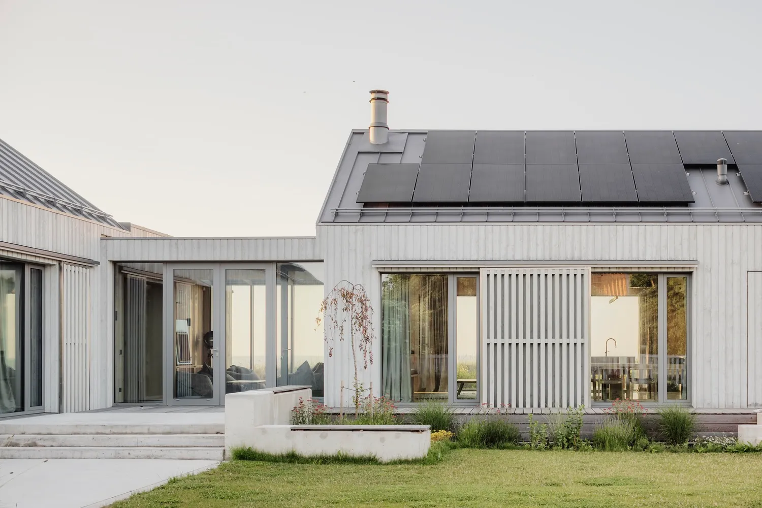 Modern residential building with rear yard featuring concrete deck and steps, solar panels on the roof, and green grass.