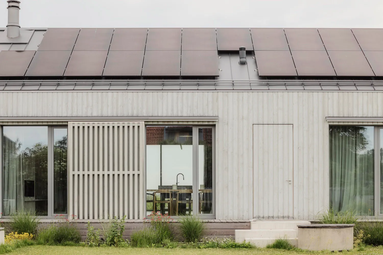 一座現代簡約的住宅建築,外牆採用木質板材,屋頂裝設太陽能板。