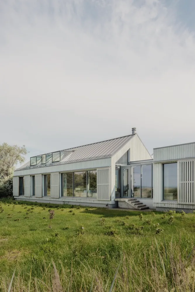 A modern residential house with glass walls and a metal-clad exterior.