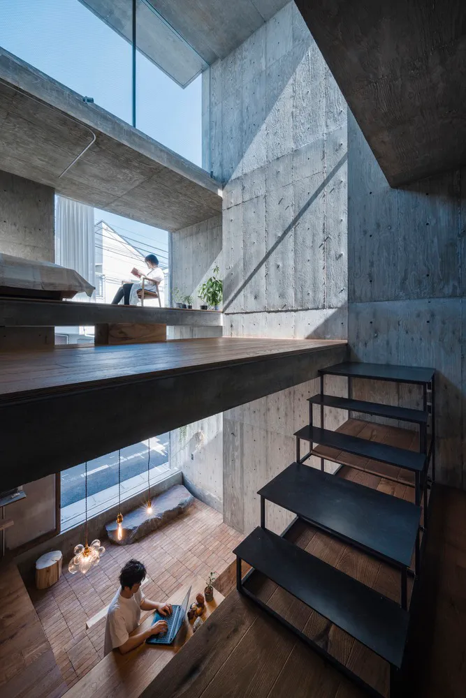 A minimalist living room with concrete walls and stairs leading down to a wooden floor.