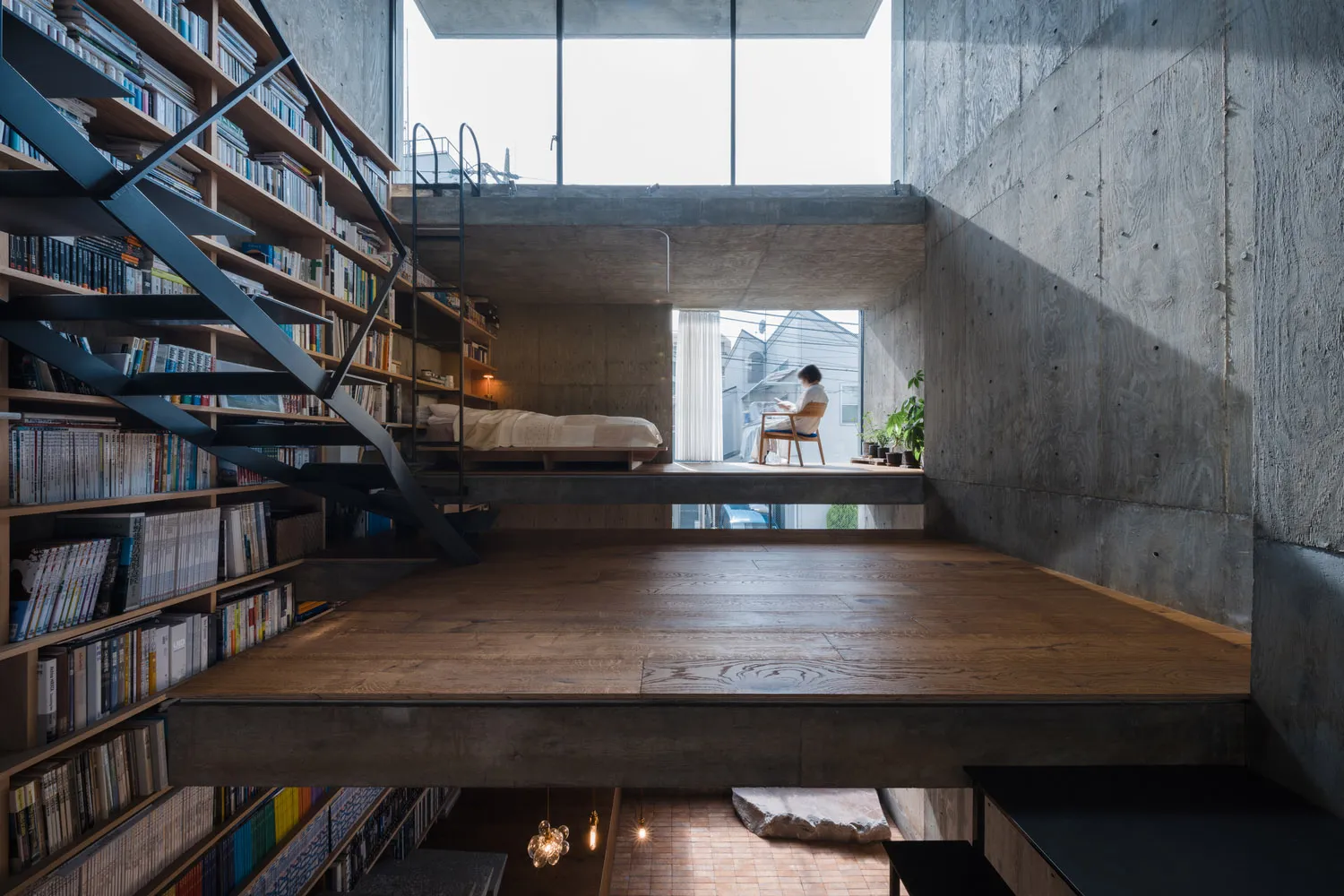Minimalist residential interior featuring concrete and wood materials, with a person sitting at a window.