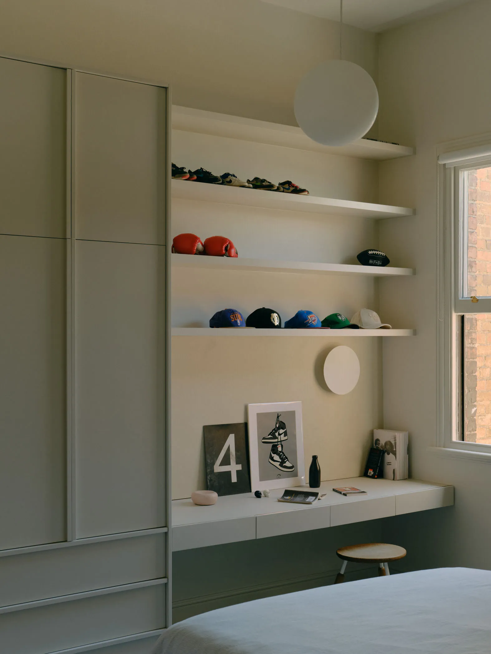 A minimalist bedroom with white shelves displaying various items like shoes, hats, and a poster of sneakers.