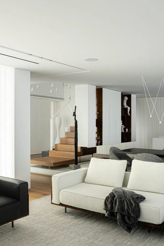 Modern minimalist living room with white couch, black armchair, and wooden accents.