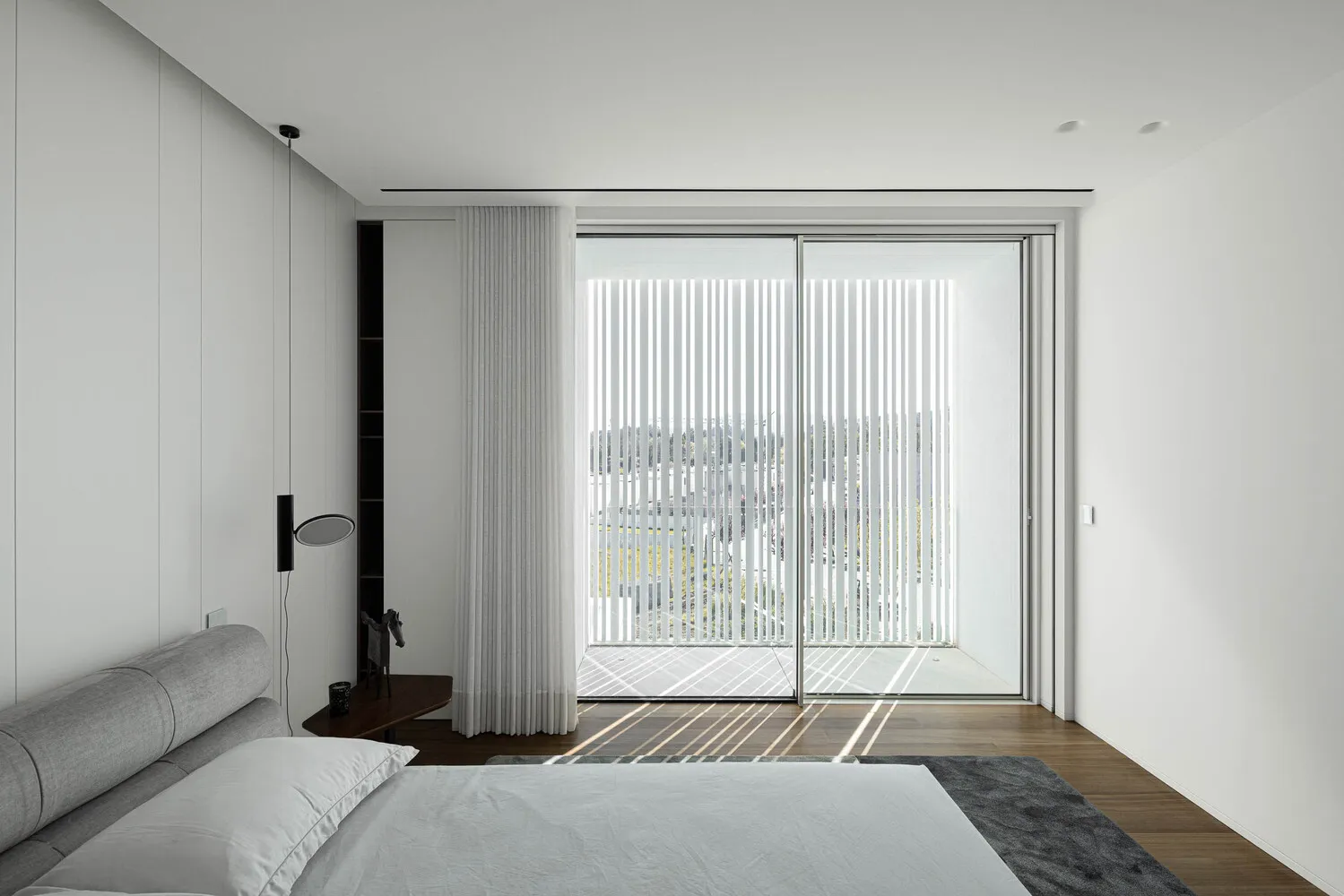 A modern bedroom featuring a white sliding glass door, minimalist furniture, and light-colored materials.