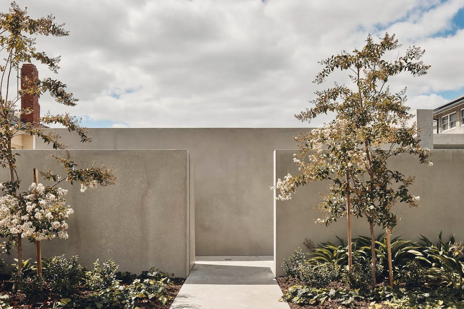 Concrete walls and pathway with flowering trees in a landscaped area.