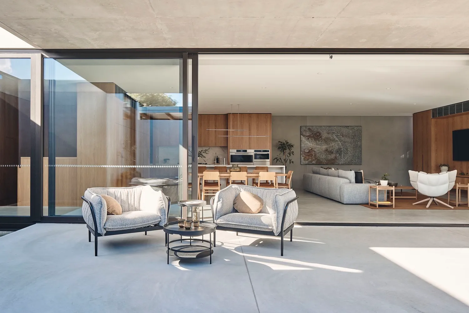 A modern living room featuring a concrete floor and furniture, with a view into the kitchen area.