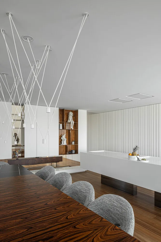 A modern living room featuring a large wooden table surrounded by upholstered chairs, a bookshelf with sculptures, and a cont