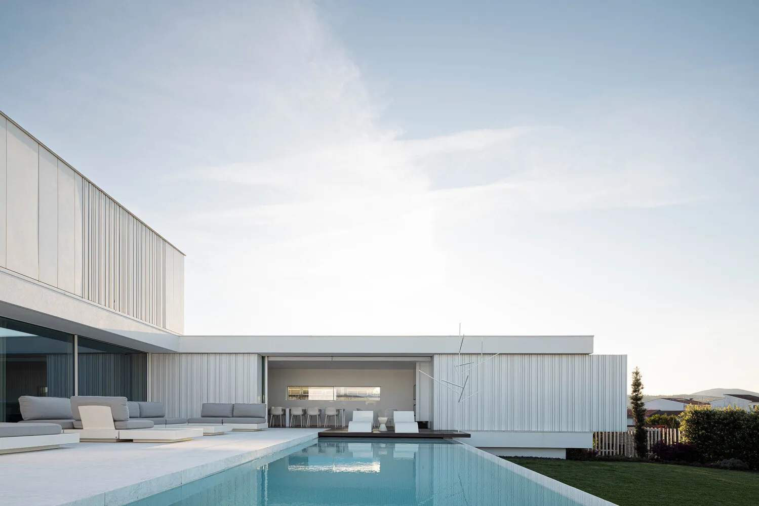 Modern white minimalist residential exterior with swimming pool and outdoor seating area.