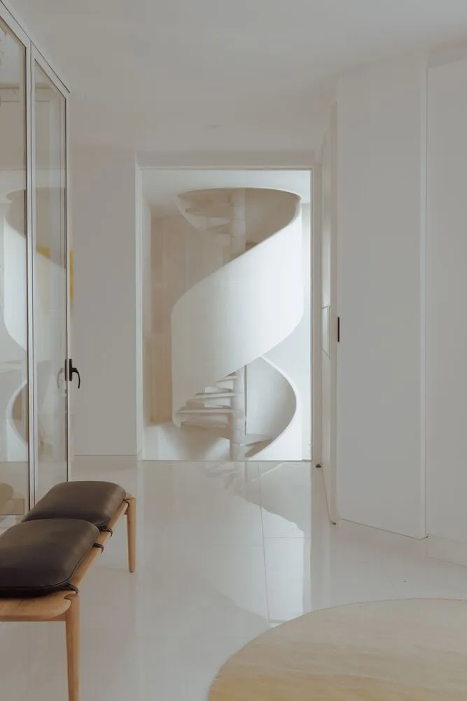Modern spiral staircase with white marble steps surrounded by glass railings and walls.