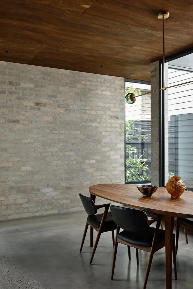 A modern industrial dining room featuring exposed brick walls, a wooden dining table, and black chairs.