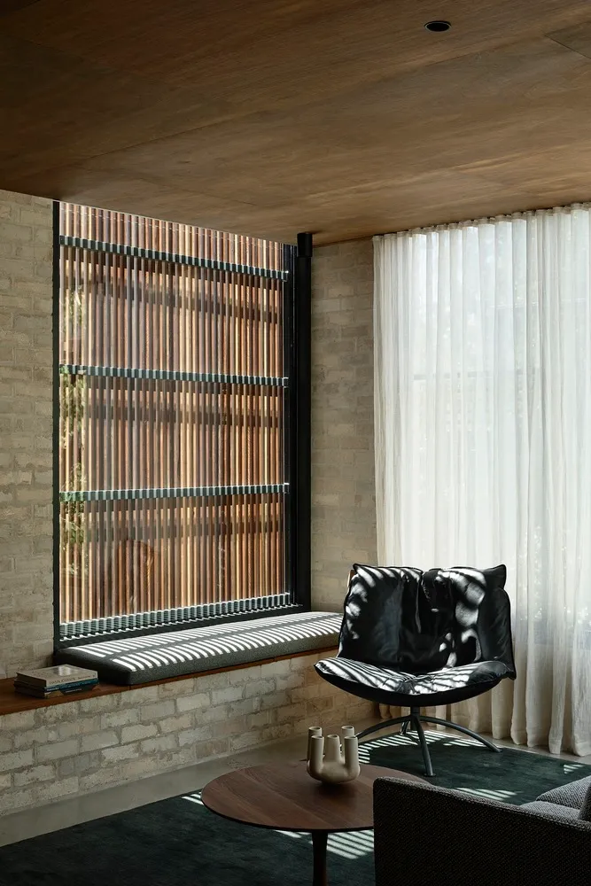 Modern living room with brick walls and wooden blinds, featuring a black lounge chair and coffee table.