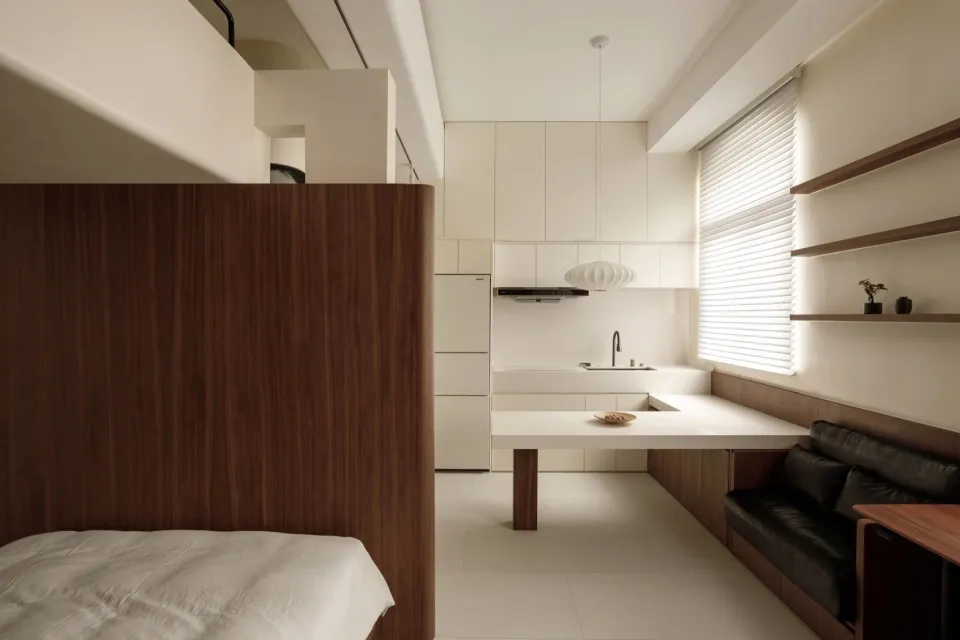 A modern, minimalist kitchen with white laminate countertops and backsplash, featuring a white refrigerator and a small dinin