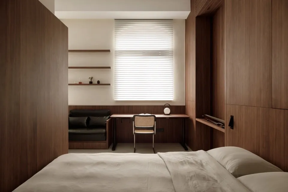 A modern minimalist bedroom with wooden walls, a bed, a desk, and a window with blinds.
