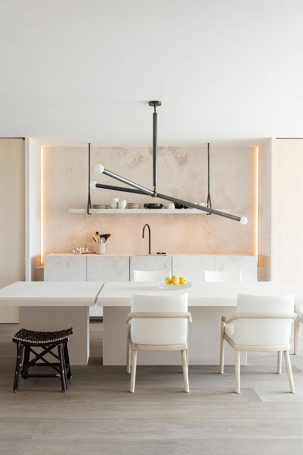 Modern minimalist kitchen with concrete countertops, white cabinets, and a dining table with white chairs and a black metal c
