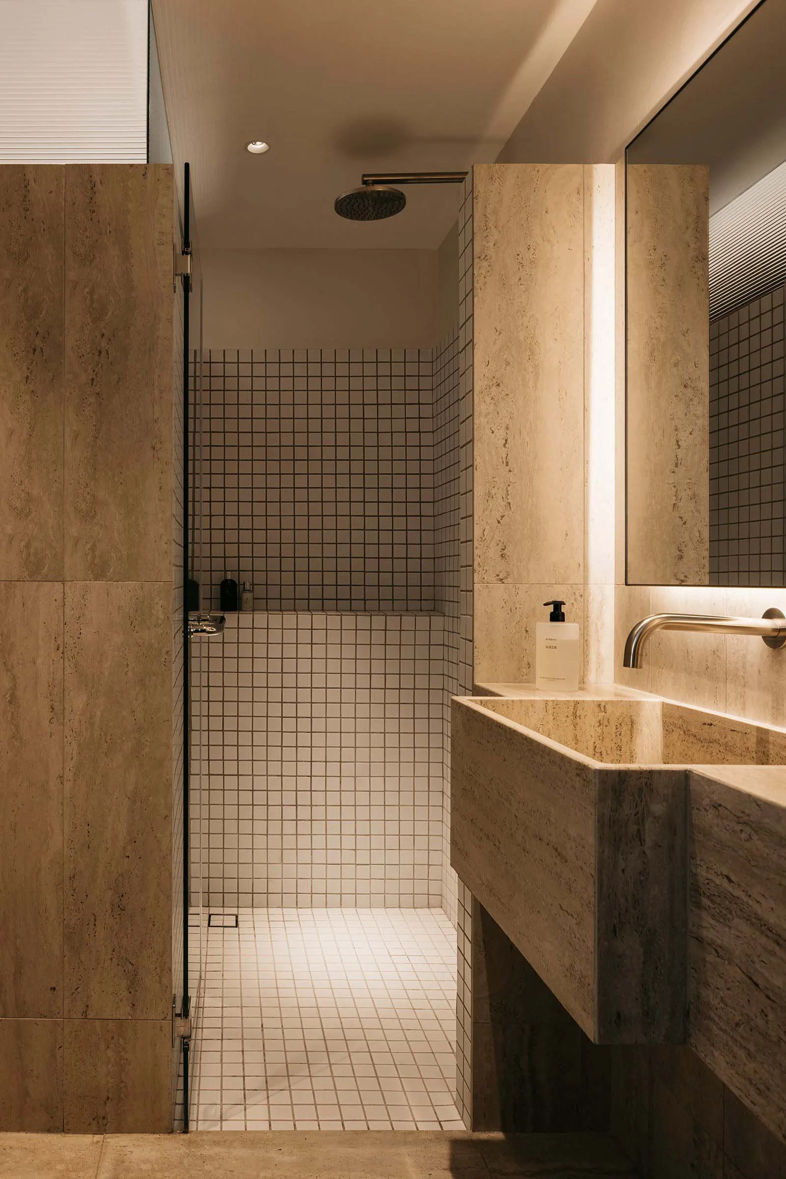 A minimalist bathroom with white tiles and marble accents, featuring a walk-in shower and a modern sink.