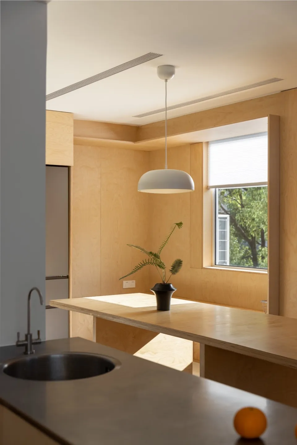 A minimalist indoor kitchen with wooden panels and a white pendant light hanging above a counter.