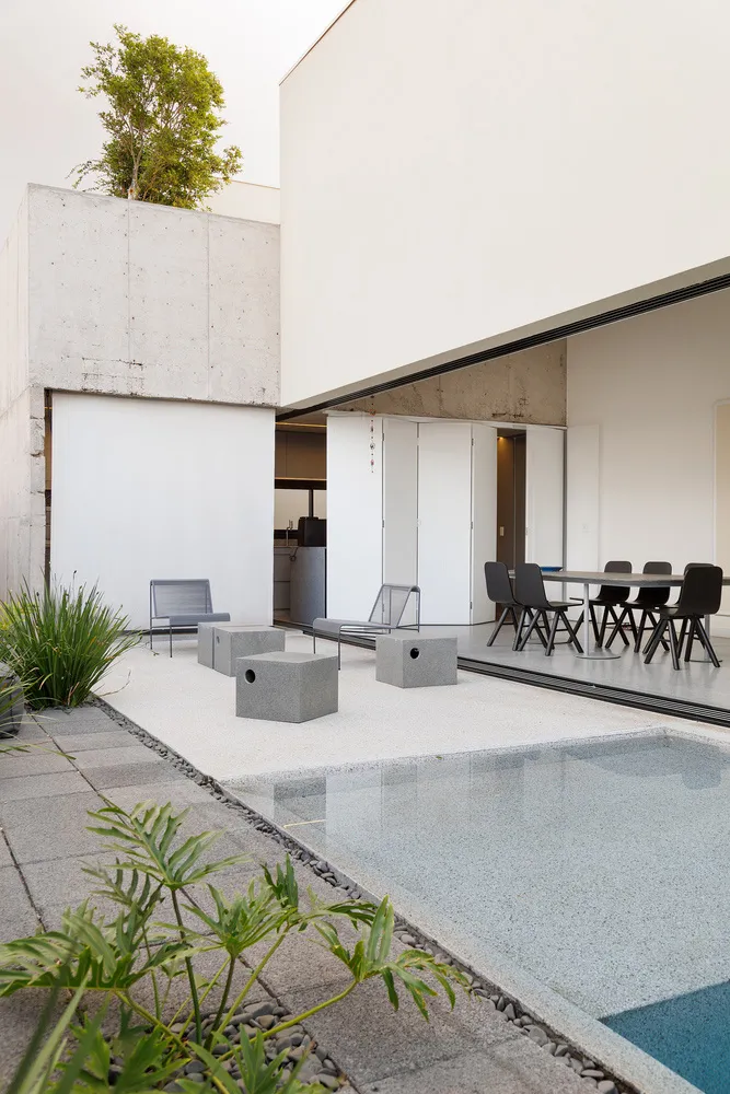 A minimalist patio with concrete furniture and a swimming pool, with a modern building in the background.