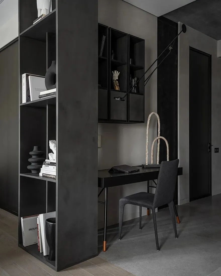 Close-up of a minimalist home office with black metal desk, chair, and shelving unit.