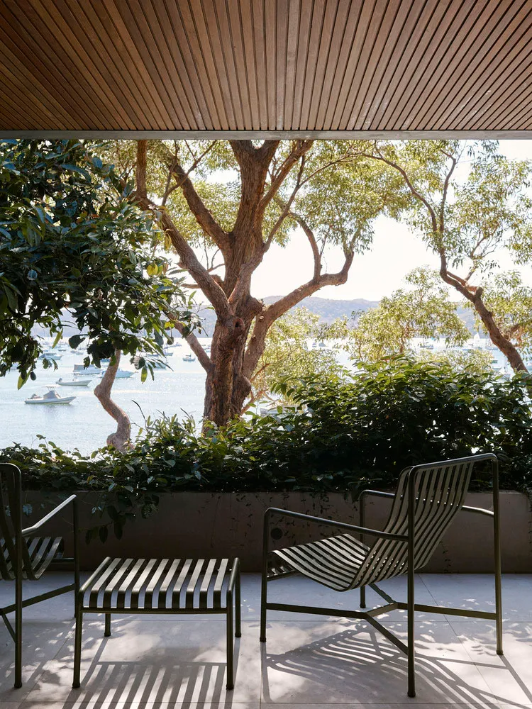 Outdoor patio lounge area with striped garden chairs, lush greenery, and a scenic water view.