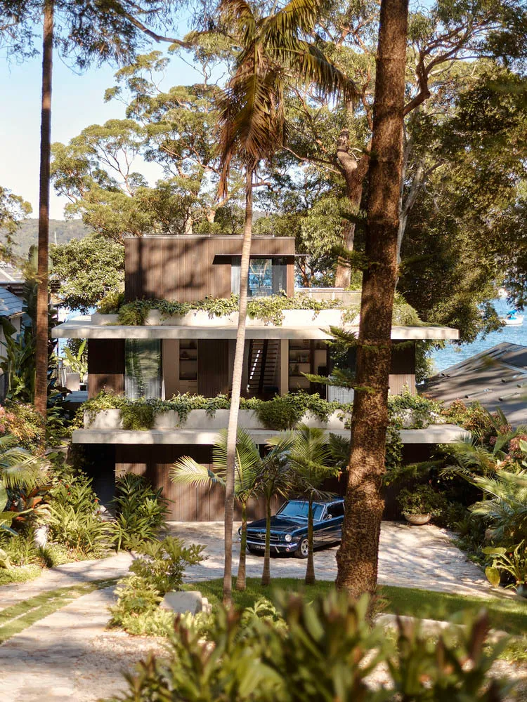 A modern house with a rooftop garden, surrounded by trees and greenery, featuring a blue car parked in the driveway.