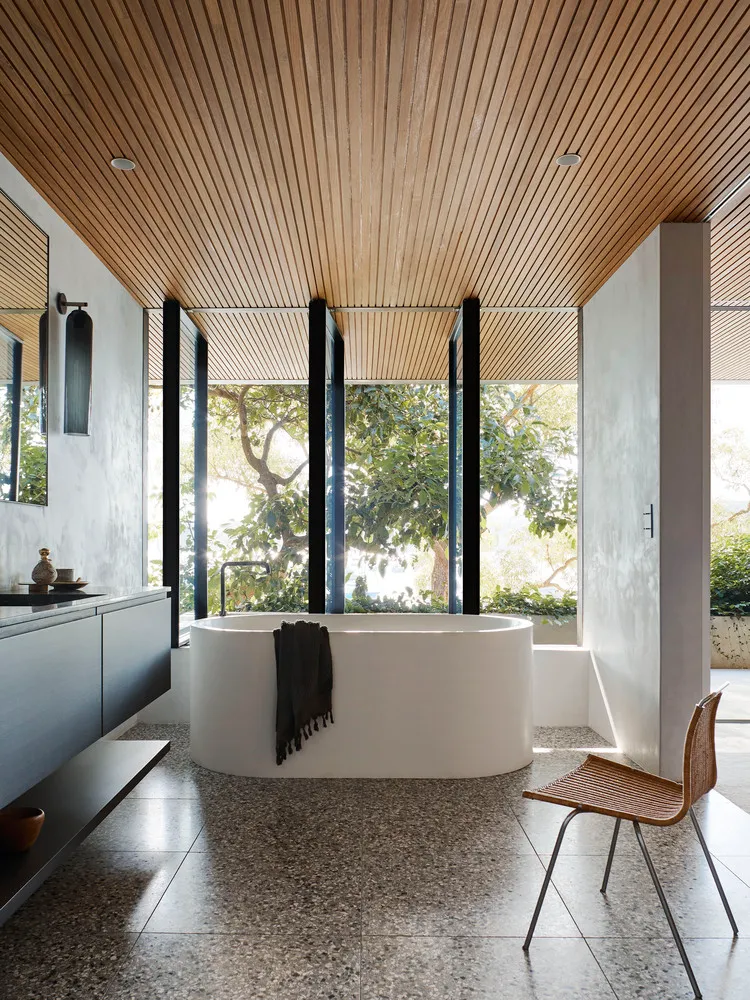 Modern minimalist bathroom featuring concrete walls, a freestanding bathtub, and wooden ceiling.