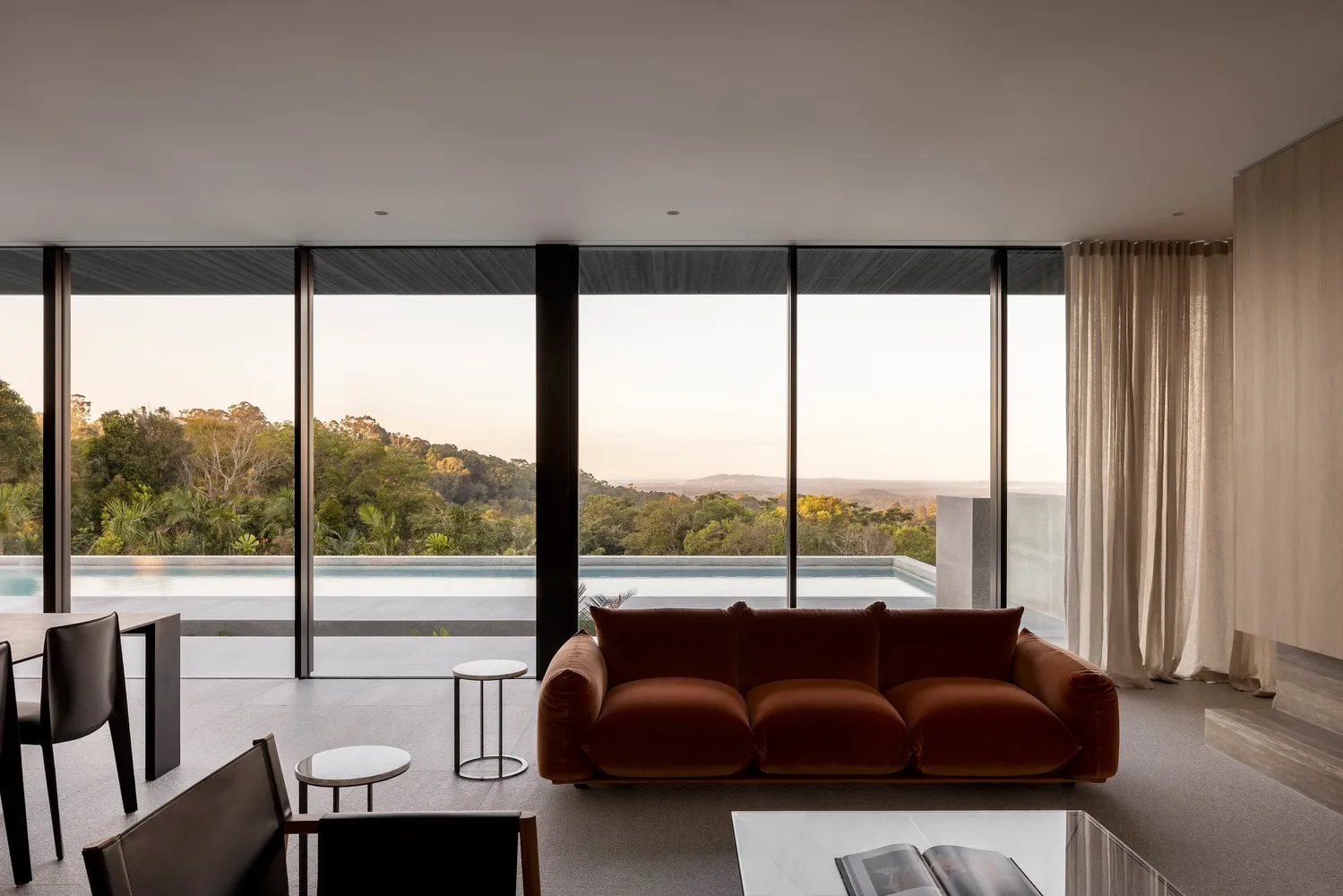 A contemporary living room featuring a glass wall overlooking a scenic landscape with a concrete floor and minimalist furnish