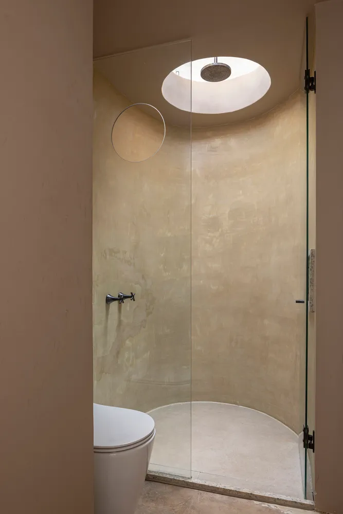 A minimalist bathroom featuring a concrete shower enclosure, circular skylight, and a white toilet.