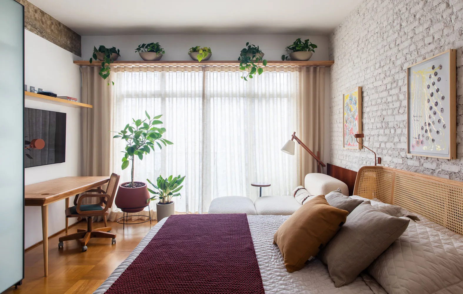 A minimalist bedroom featuring wooden furniture and textiles, with a large window allowing natural light.