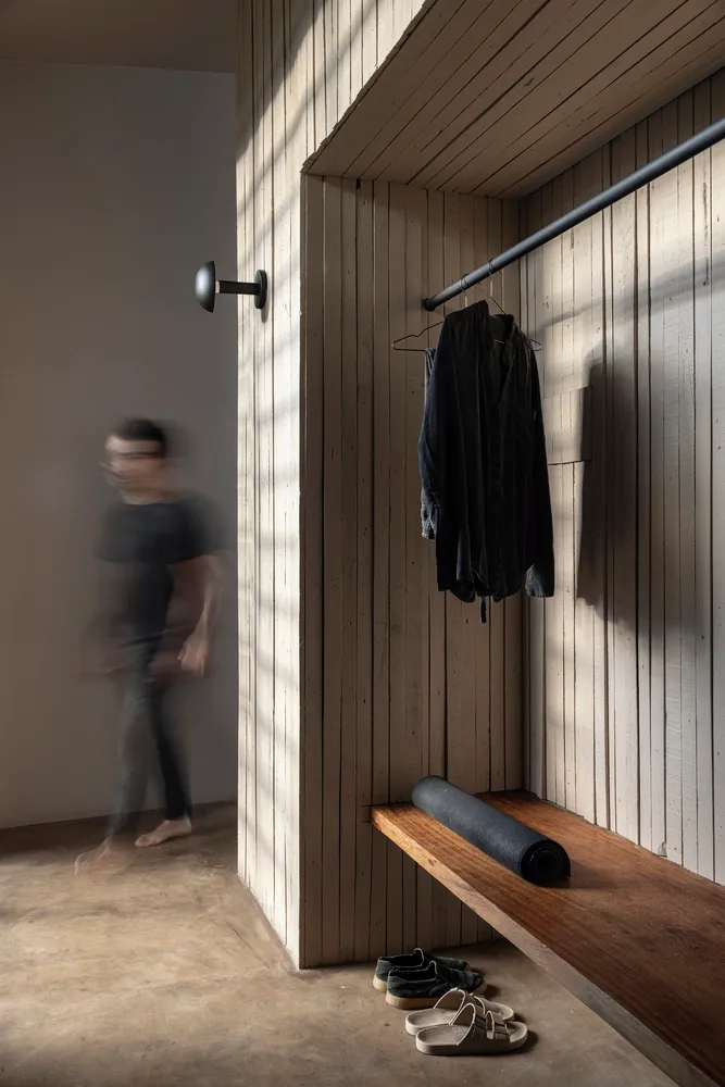 A minimalist entryway featuring a wooden bench, yoga mat, and hanging clothing.