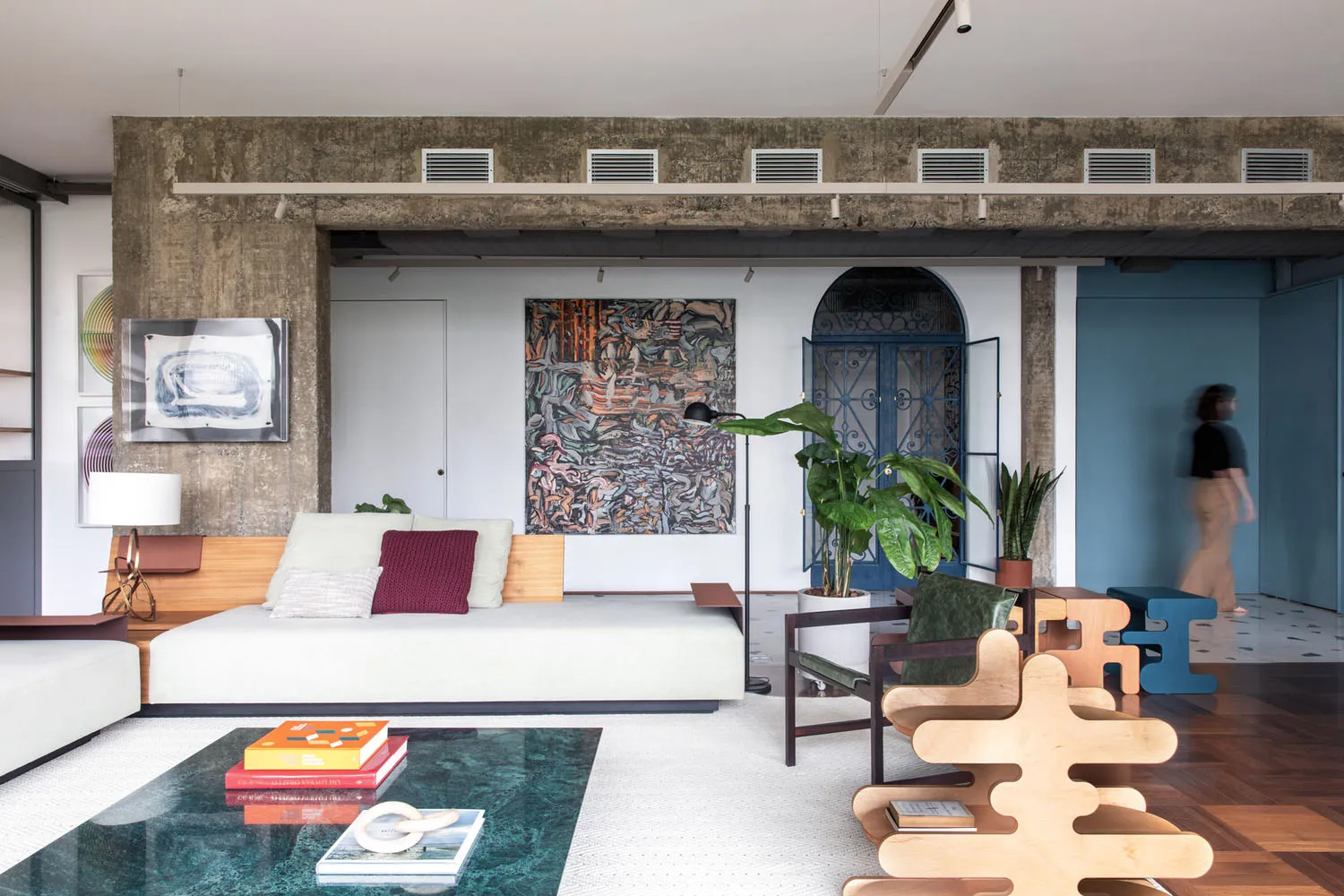 A modern living room features a white sofa with wood accents, artworks on the wall, plants, and a glass coffee table.